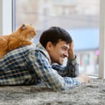 Young man with fluffy cat lying on a carpet